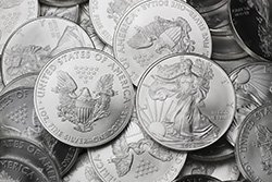 Produktmix American Eagle Silbermünzen ältere Jahrgänge vor 2021 Einige Silbermünzen liegen durcheinander auf einer Stelle. Mittig stechen zwei heraus, sie zeigen als Motive je die Lady Liberty und das Große Siegel der Vereinigten Staaten mit einem Adler.